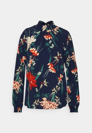 Blusa azul-marinho com mangas longas e gola alta com volantes, com um padrão floral em vermelho, creme e verde sobre um fundo escuro.
