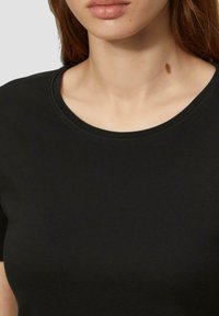 T-shirt nero a maniche corte realizzato in tessuto liscio, con scollatura rotonda e un accentuato dettaglio testurizzato vicino al colletto.