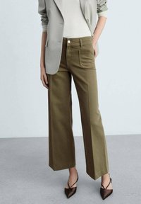 Pantalon large vert olive en tissu de coton. Comprend deux poches avant, une fermeture à bouton et une coupe ajustée. Assorti à un blazer léger.