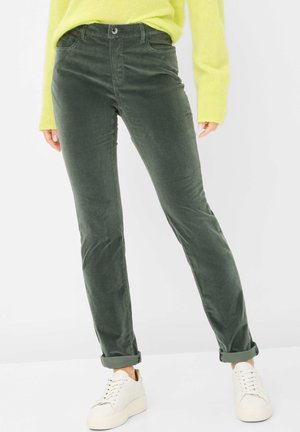 Pantalons en velours côtelé verts à coupe slim, dotés de poches avant et de poignets retroussés, associés à des baskets blanches et un pull jaune vif.