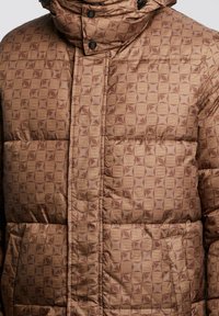 Puffer jacket in a warm brown, featuring a geometric pattern in lighter shades, a high collar, and snap closures for secure fastening.