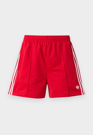 Punased sportluspüksid elastse vöökohaga, kahe külje luku taskuga, valgete triipudega külgedel ja väikese Adidas logo ees paremal reiel.