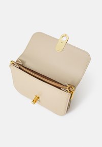 Borsa a mano in pelle beige con hardware dorato, chiusura a doppio ribaltabile e tasche interne. Texture liscia con un design minimalista.