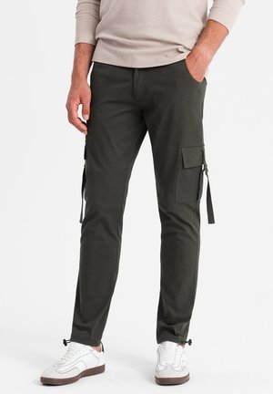 Tmavě zelené cargo kalhoty vyrobené z bavlněné směsi, s bočními kapsami, staženými manžetami a slim fit designem. Nosené s bílými teniskami.