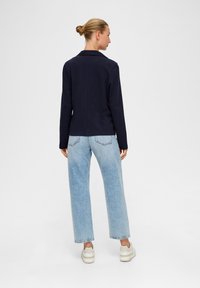 Granatowa kurtka o strukturalnym kroju, zestawiona z jasnoniebieskimi spodniami o szerokich nogawkach. Stylizacja ma swobodny charakter oraz schludne wykończenie.