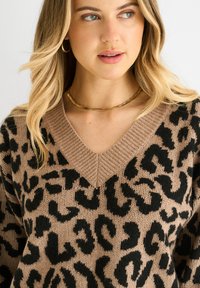 Knit sweater in beige with a black leopard print, featuring a V-neck and ribbed neckline. Soft texture and loose, comfortable fit.