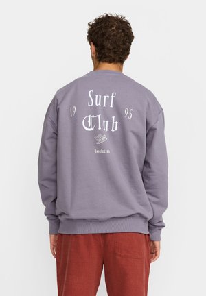 Paarse sweatshirt met een grote witte afbeelding met de tekst "Surf Club", "1995" en een surfplankontwerp; geribbelde manchetten en zoom, ontspannen pasvorm.