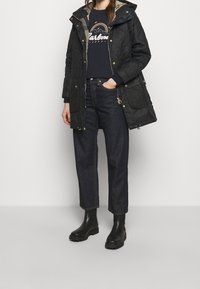 Prošívaná černá parka s kapucí, doplněná o námořnickou grafickou mikinu, tmavé džíny a černé gumové kotníkové boty.