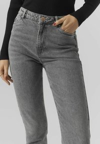 Jeans de mezclilla gris de cintura alta con un clásico diseño de cinco bolsillos, un sutil desgastado y un botón de cobre en la cinturilla.