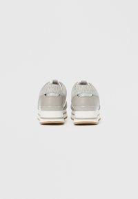 Par beige og hvide platform-sneakers med "Michael Kors" branding på hælen og MK-mønster på øvre bagside, set bagfra.