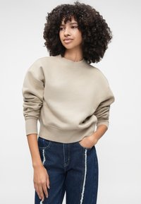 Hanorac bej cu guler rotund, umeri căzuți și manșete ribbed, combinat cu blugi din denim închis, cu cusătura laterală desfăcută.