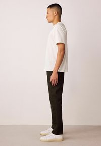 Valge lühikeste varrukatega t-särk, peen must püksid ja valged tossud. Kangas näeb välja sile; lõige on kaasaegne ja kohandatud.