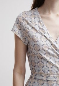 Ručně šitá zavinovací šaty s květinovým vzorem v světlých béžových a modrých odstínech. Mají krátké rukávy a hluboký výstřih do V, vyrobené z měkkého, texturovaného materiálu.