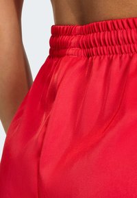 Crvene satenske hlačice s naboranim elastičnim strukom i glatkom teksturom, naglašavajući živopisnu jednobojnu boju s blagim sjajem.