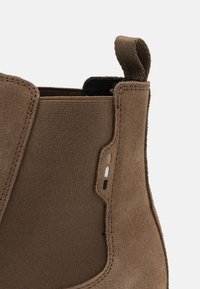 Hnědé semišové Chelsea boty s elastickým bočním panelem a poutkem, obsahující malé vyšívané detaily v béžové, bílé a černé barvě.