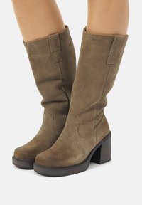 Kniehoge bruine suède laarzen met een blokhak, voorzien van een zijrits en decoratieve stiksels. Glad oppervlak met een stevige zool.