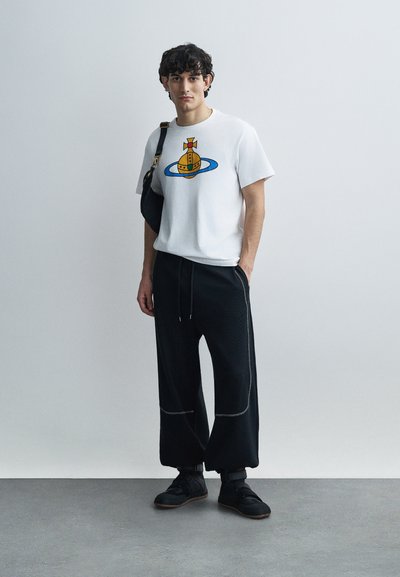 Λευκό T-shirt με μπλε και κίτρινο γραφικό σχέδιο, συνδυασμένο με μαύρο παντελόνι φαρδιάς γραμμής με υφή και γκρι ραφές.