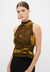 Top halter floreale marrone con colletto alto, texture trasparente e dettagli plissettati. Abbinato a una gonna nera aderente. Orecchini a cerchio dorati.