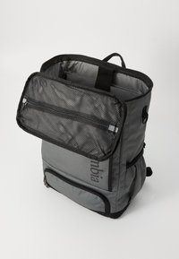 Gray backpack with a mesh zippered top pocket, front zip compartment, and padded side sections. Features straps and a carry handle.