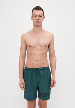 Dark green swim shorts with an elastic waistband and drawstring. Features a large black "BORG" print on the left side. Smooth, lightweight fabric.