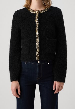 Schwarzer, strukturierter Cardigan mit langen Ärmeln und zwei Fronttaschen, verziert mit gold- und silberfarbenen Paillettenbändern entlang des Halsausschnitts und des Knopfbereichs.