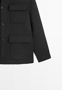 Donkergrijze wollen jas met twee voorkruiken, knoopsluitingen en een iets gestructureerde silhouet. Gladde textuur met een nette afwerking.