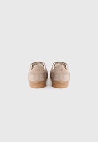 Sneakers in suede beige con suole in gomma marrone, caratterizzati da una forma arrotondata e un design minimalista. Marchio visibile sul tallone.