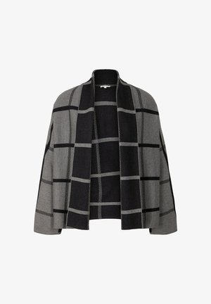 Zwarte broek met wijde pijpen gecombineerd met een grijs-zwart geruite cardigan met een geribbelde textuur en een aansluitende coltrui eronder. Zwarte loafers.