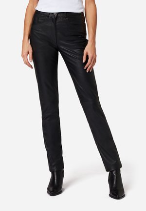 Zwarte leren broek met een slim fit, voorzien van een rits aan de voorkant, vijf zakken en gestikte details op de knieën, gecombineerd met zwarte haklaarzen.