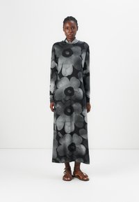Long-sleeved black dress with large gray floral pattern, made of a soft fabric. Paired with brown strappy sandals.