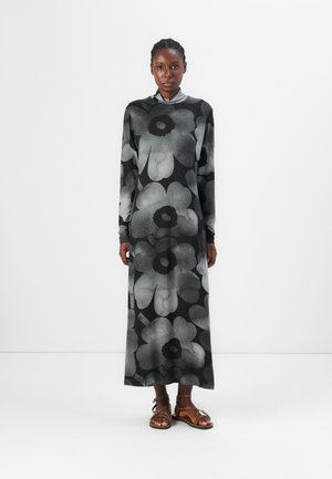 Robe noire à manches longues avec un grand motif floral gris, fabriquée dans un tissu doux. Assortie à des sandales à lanières marron.