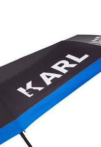 Zwarte en blauwe paraplu met een groot wit "KARL" logo, voorzien van een gladde stoffen canopy en een slank ontwerp. De handgreep is stevig en functioneel.