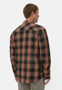 Sort, rød og orange ternet flannel skjorte med lange ærmer, knapmanchetter og en let buet kant. Har en klassisk krave og rygskulder.