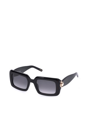 Lunettes de soleil rectangulaires noires avec des montures épaisses et des verres dégradés foncés, avec un petit détail circulaire doré sur chaque branche.