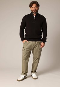 Zwarte ziptrui, kaki cargo shorts met zijzakken en witte sneakers met zwarte accenten. Glad textuur, casual ontwerp.