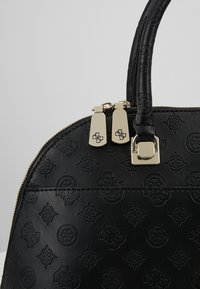 Sac à main en cuir noir avec motifs géométriques embossés, tirettes de fermeture éclair dorées gravées de logos, et poignée cousue courbée.