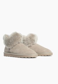 Bottes chelsea en daim beige avec des poignets en fourrure douce et duveteuse, semelles en caoutchouc plates et design de bout arrondi et lisse.