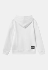 Sudadera blanca con capucha ajustable, puños de canalé y corte corto. Presenta una etiqueta rectangular negra con la palabra "JEANS" en la parte posterior.
