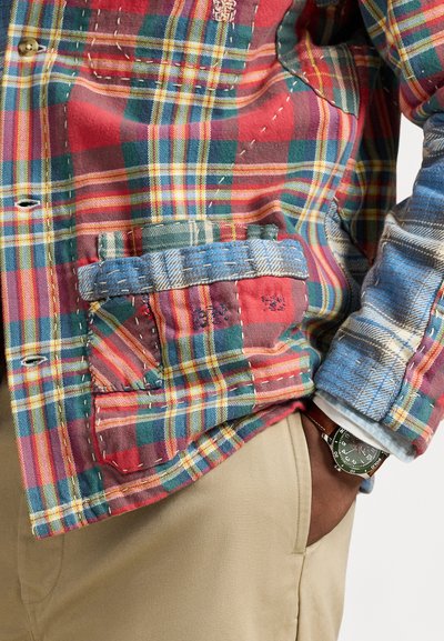 Καρό πουκάμισο σε αποχρώσεις του κόκκινου, πράσινου και κίτρινου, με διάφορες λεπτομέρειες από πατς, με μπλε τόνους στην τσέπη και αντιθετικές υφές.