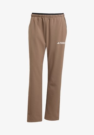 Pantalons de sport marron avec une taille élastique, jambes droites et un logo blanc "TERREX" sur la cuisse gauche. Texture de tissu lisse.
