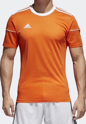 Mann trägt ein oranges Adidas-Sporttrikot mit weißen Streifen auf den Schultern und weiße Shorts, steht mit entspannten Armen.