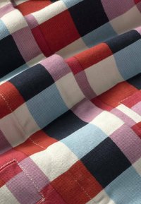 Tissu en coton avec un motif à carreaux coloré composé de carrés rouges, blancs, noirs, bleus et violets, montrant des coutures et des plis visibles.