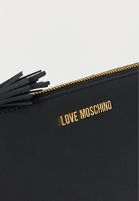 Μαύρο δερμάτινο τσαντάκι με εξαρτήματα σε χρυσή απόχρωση. Διαθέτει φερμουάρ και διακοσμητική μαύρη φούντα. Εμφανίζεται το λογότυπο "LOVE MOSCHINO" χαραγμένο.
