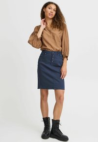 Brun texturerad blus med puffärmar, matchad med en figursydd marinblå denimkjol med en framsidesknapp och svarta bekämpningsstövlar.