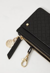 Portefeuille en cuir tissé noir avec zip et quincaillerie dorés, présentant un charme décoratif et une surface texturée pour un détail supplémentaire.