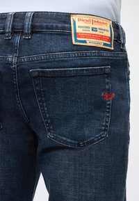Σκούρο μπλε τζιν denim από πίσω, με ορθογώνια ετικέτα "Diesel Industry" και κείμενο σχετικά με την ποιότητα και την εγγύηση στη μέση.