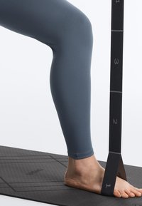 Bosá noha na jogovej podložke s čiernou elastickou odporovou páskou obtočenou okolo nohy, označenou číslami 1 až 4.