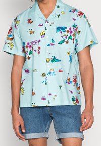 Camicia a maniche corte in cotone blu chiaro con stampe colorate e giocose di insetti e fiori; presenta una tasca sul petto e chiusura con bottoni.