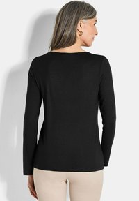 Schwarzes Langarmoberteil mit rundem Ausschnitt; körpernahe Passform und weiche Textur; von hinten betrachtet, kombiniert mit hellen Hosen.