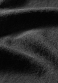 Tessuto nero strutturato con una superficie morbida e opaca, che mostra sottili variazioni nella trama e un aspetto leggermente stropicciato.